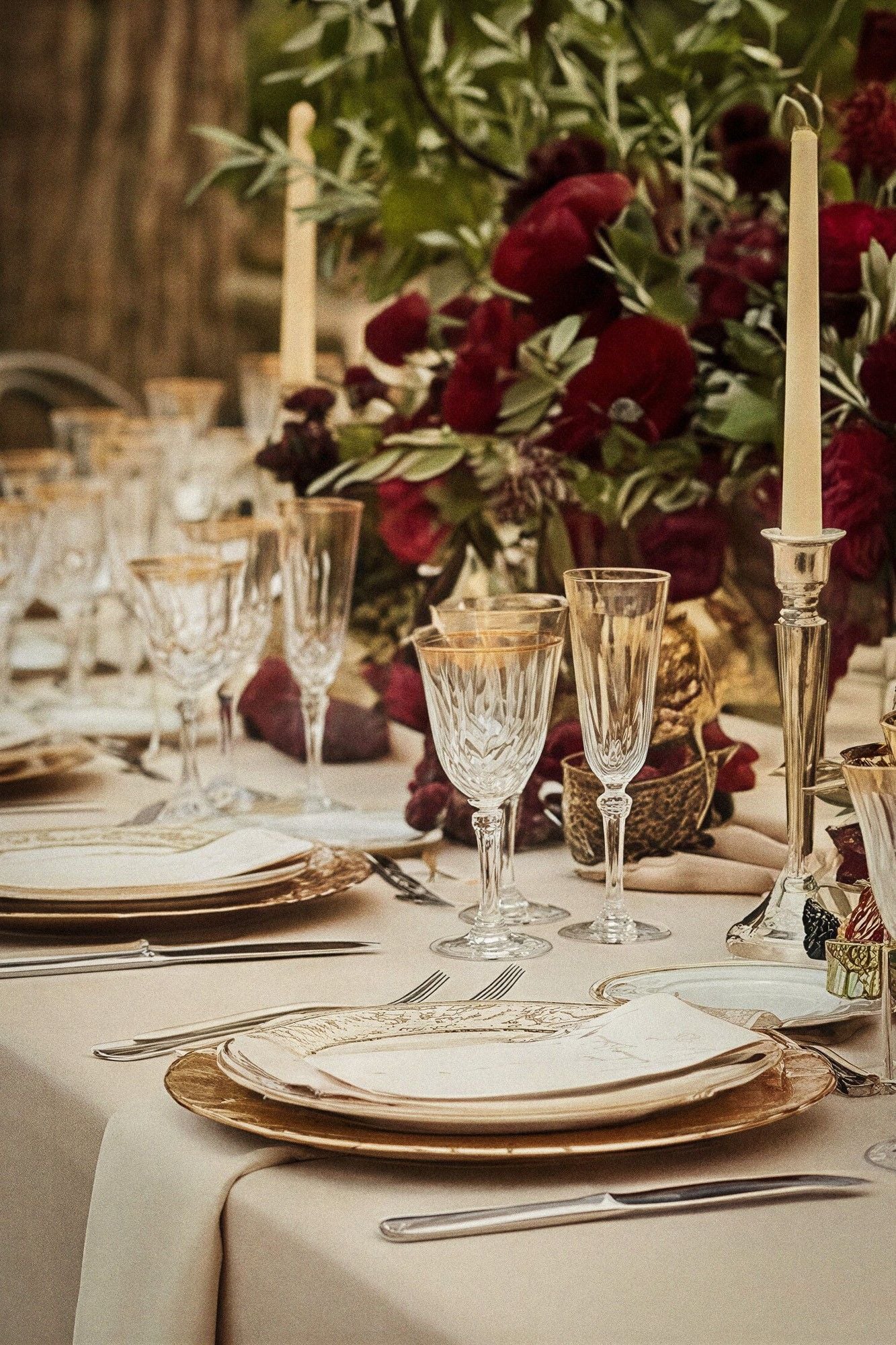A beautifully set wedding table adorned with elegant glassware, gold-rimmed plates, and lush floral arrangements.