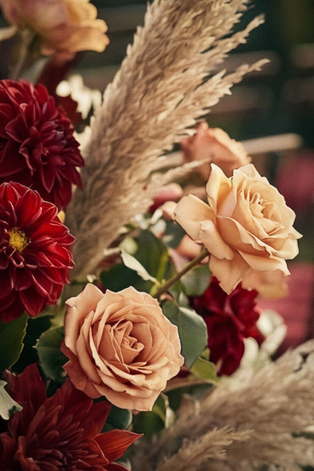 A close-up of a floral arrangement featuring peach roses and deep red dahlias, exuding a romantic and elegant ambiance.