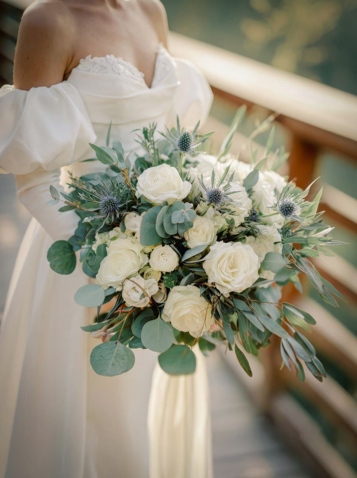 Bridal bouquet featuring white roses, thistle, and greenery, held by a bride in a romantic setting.