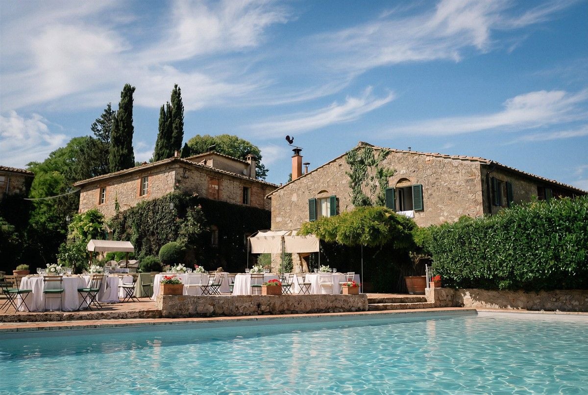 A rustic villa with a pool and elegant tables set for a wedding under a blue sky and lush greenery.