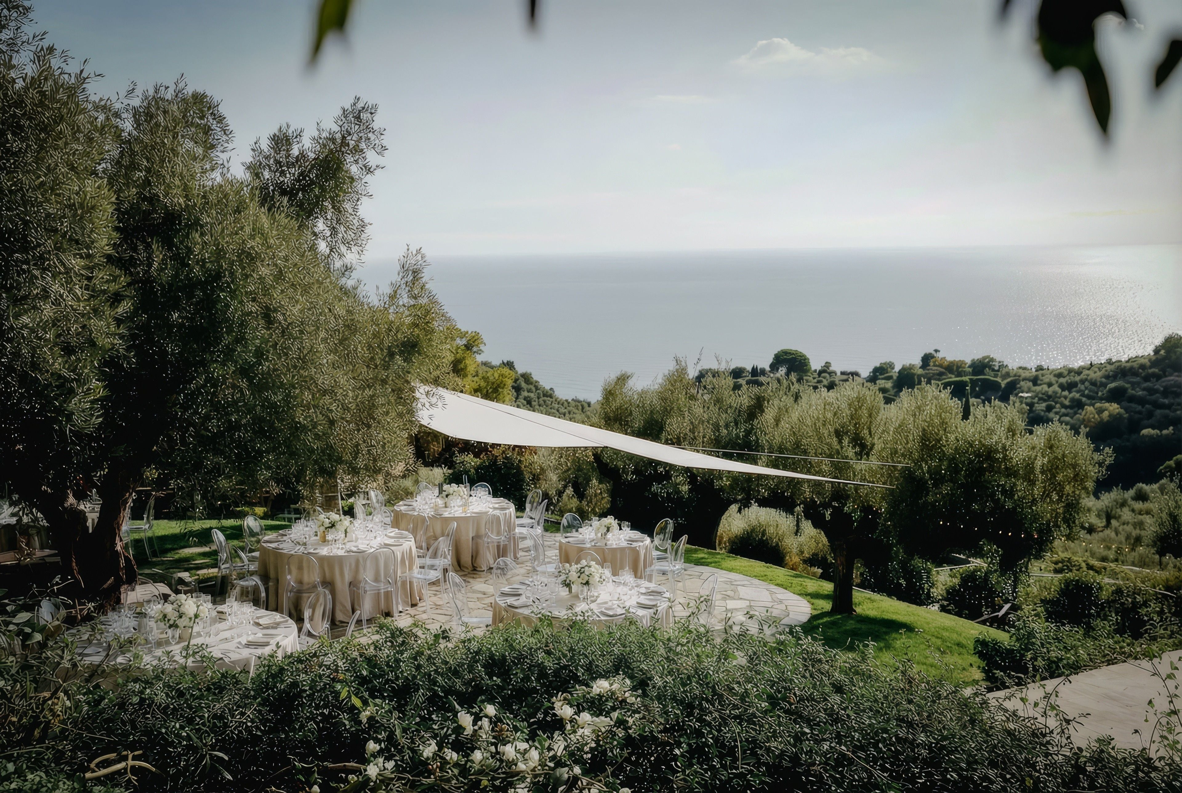 Elegant outdoor wedding setup with round tables, white linens, and a stunning ocean view under a canopy.