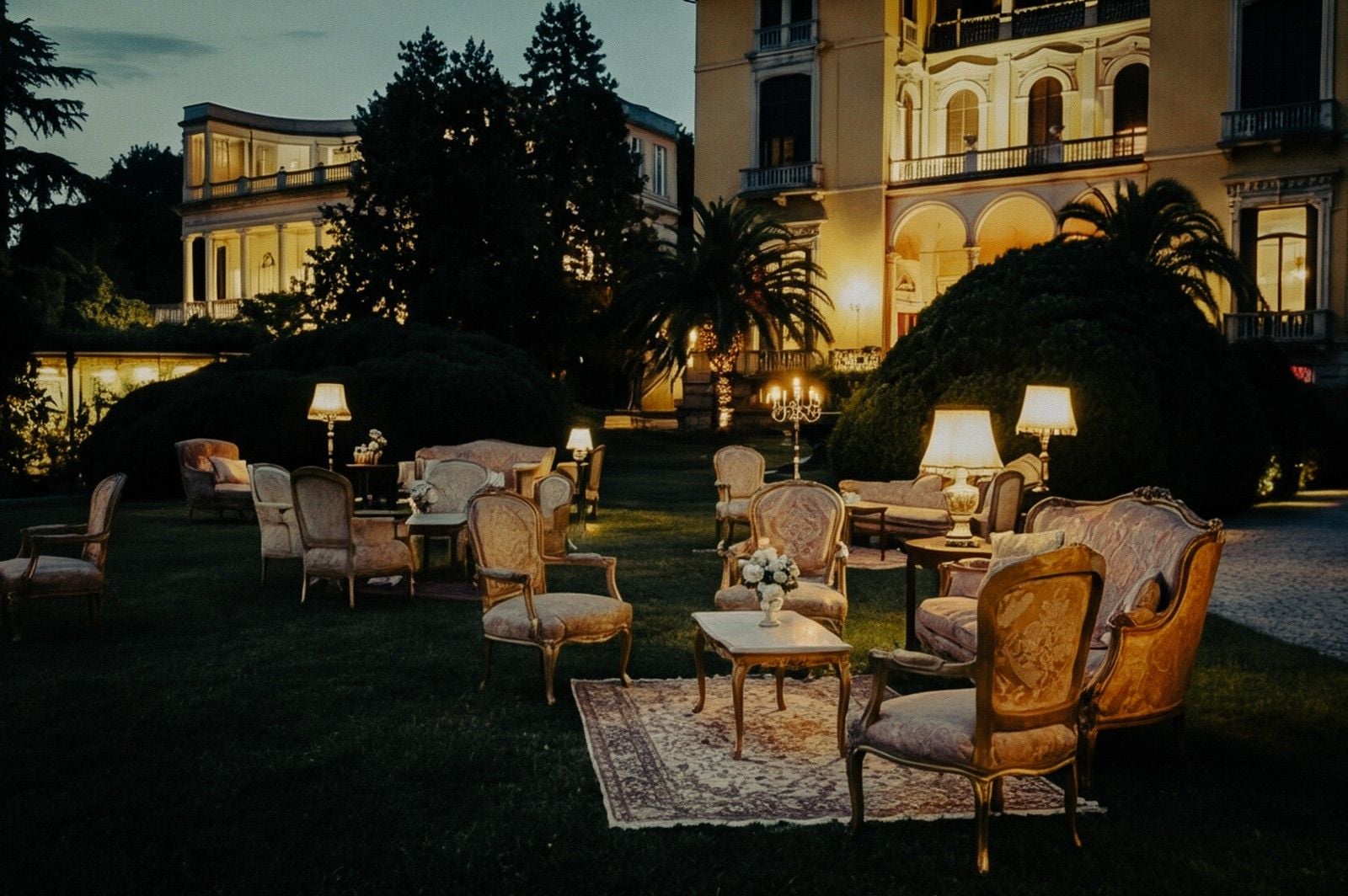 Elegant outdoor seating area at twilight, featuring vintage furniture and illuminated lamps, creating a romantic atmosphere.