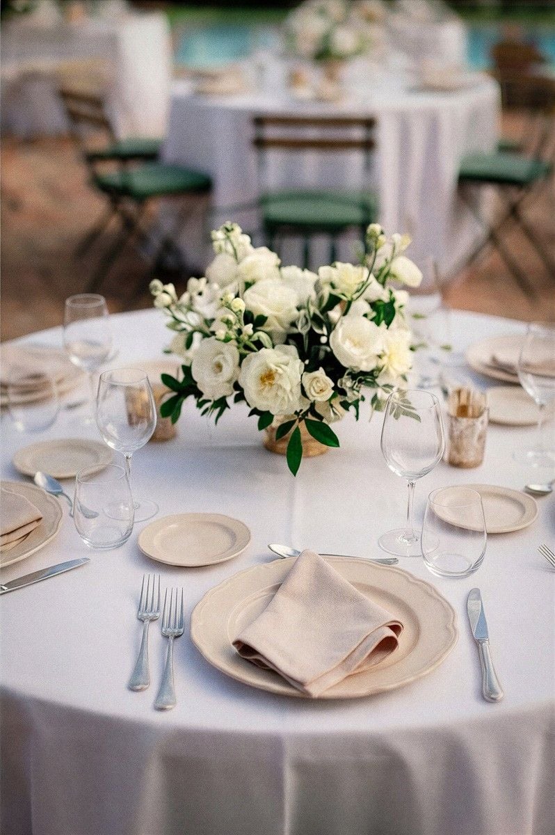 A beautifully set wedding table features elegant floral arrangements, fine china, and glassware, creating a romantic ambiance.