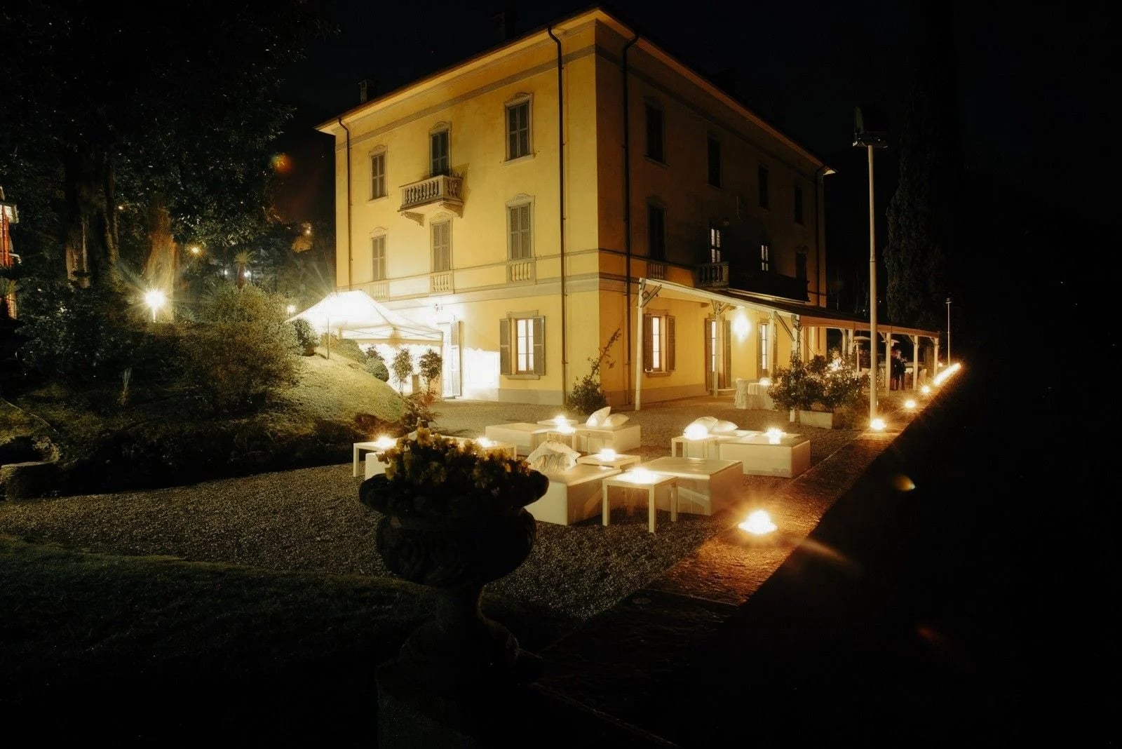 Elegant restaurant exterior at night, featuring illuminated seating area and lush garden ambiance.