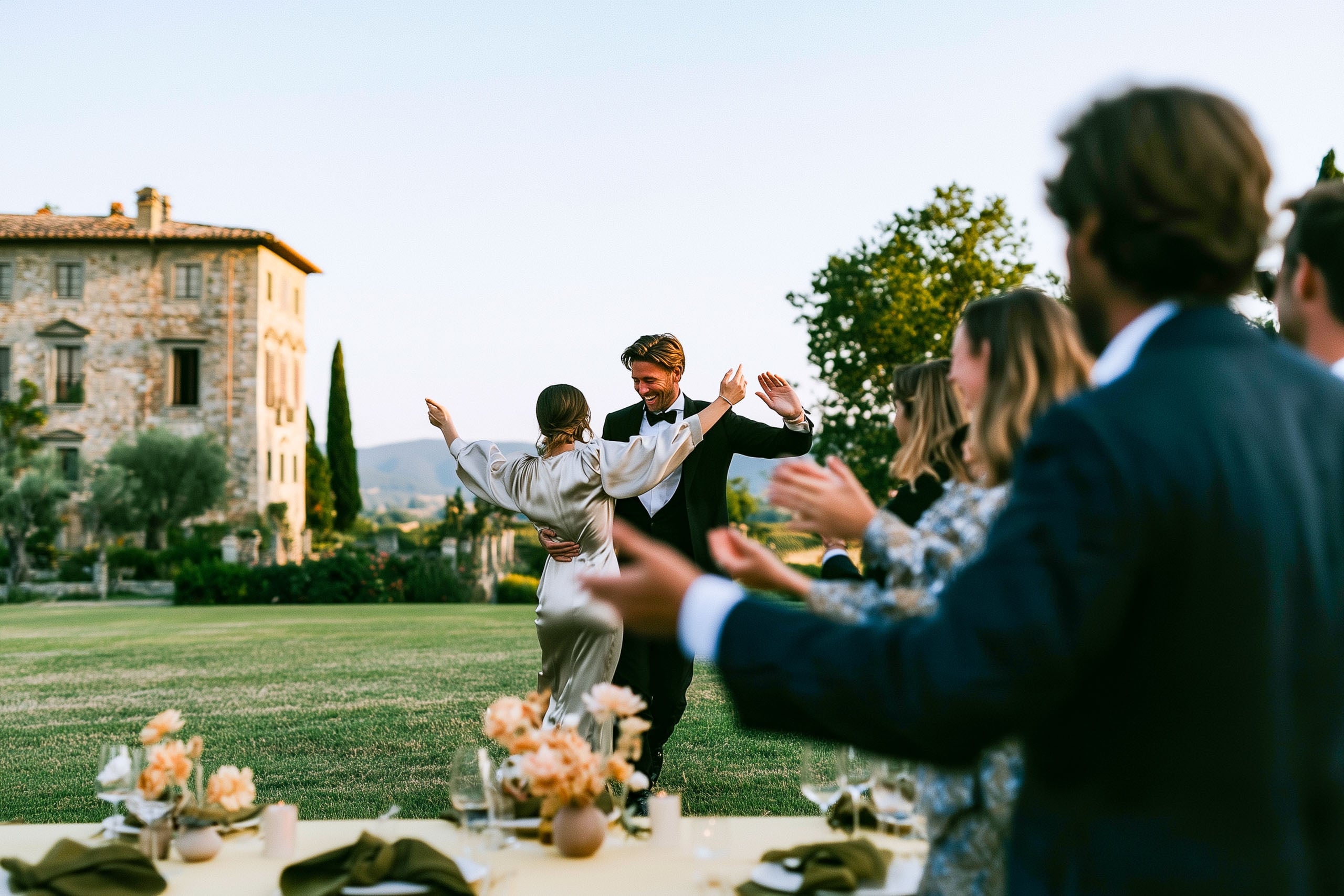 Couple dancing at their wedding in Tuscany as guests applaud, stone villa, cypresses and rolling hills behind