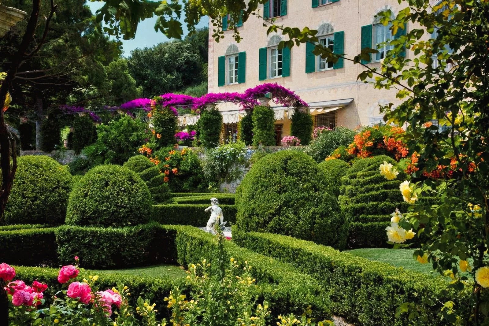 Lush garden featuring neatly trimmed hedges, vibrant flowers, and a charming statue amidst blooming greenery.