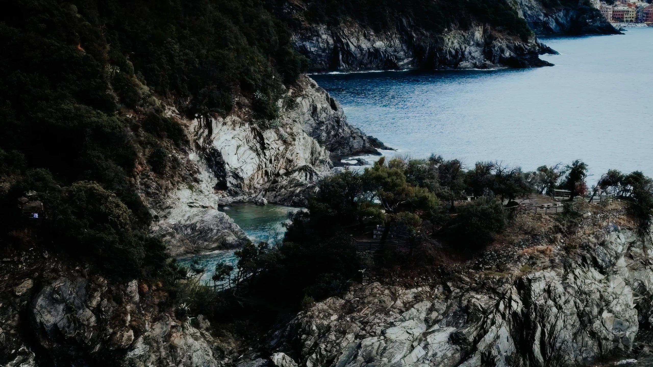 Rocky cliffs and a turquoise cove on the Cinque Terre coast, a coloured village in the distance, Liguria, Italy