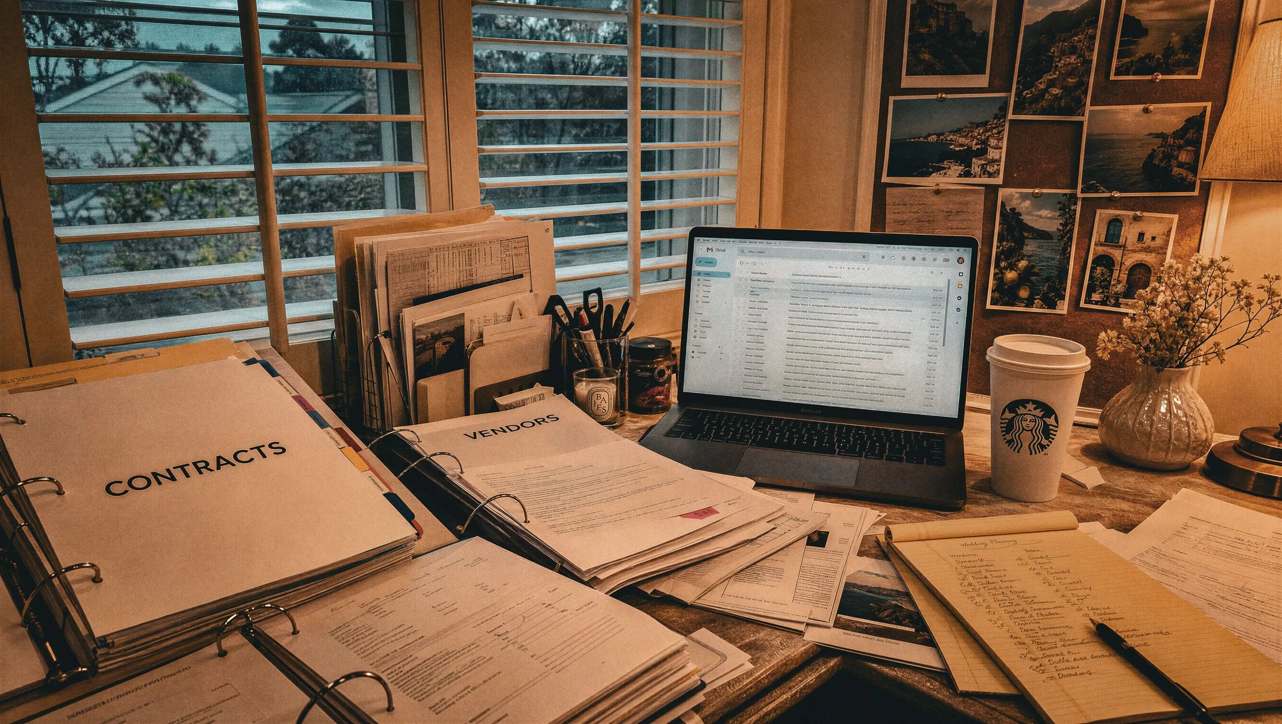 Wedding planning desk with contracts and binders, Italian photos on a pinboard in the background